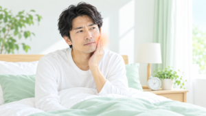 朝起きたときに歯ぎしりや食いしばりによるあごの疲れを感じている男性のイラスト